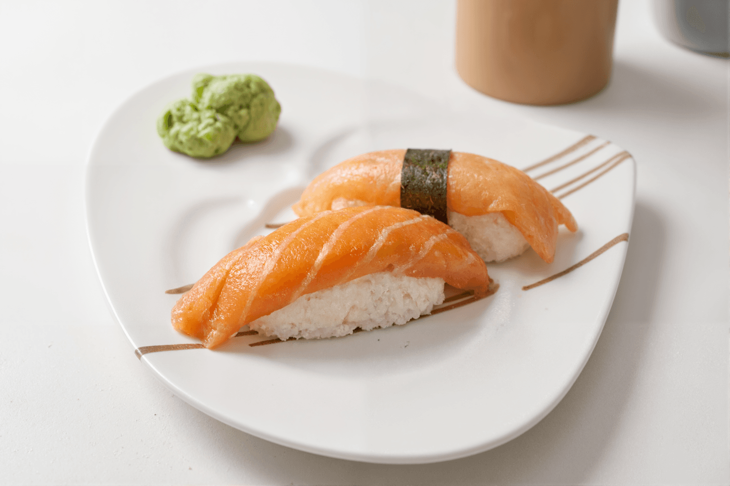 Two pieces of salmon nigiri with fresh wasabi on a white plate