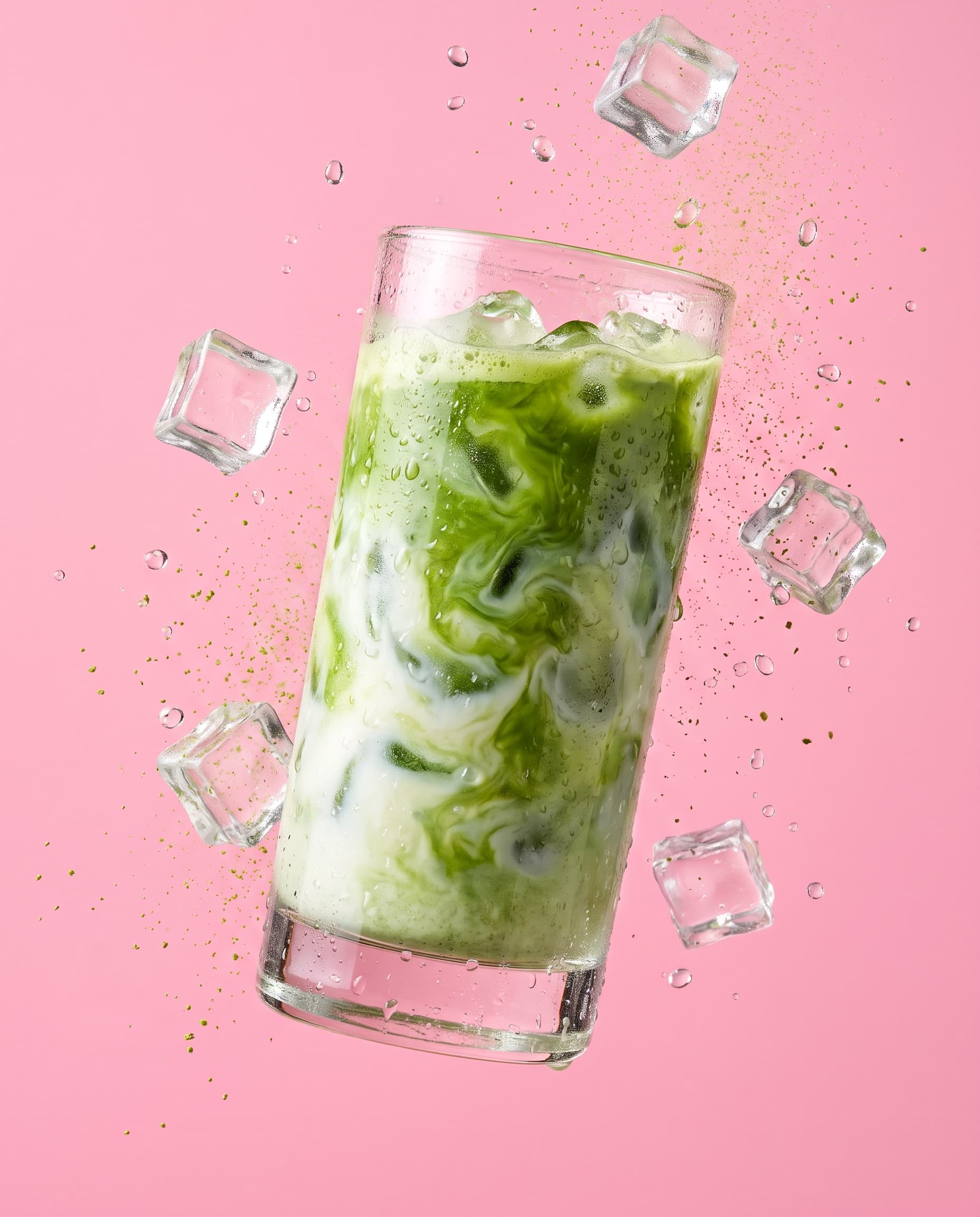 A tall glass of iced matcha latte with ice floating on pink